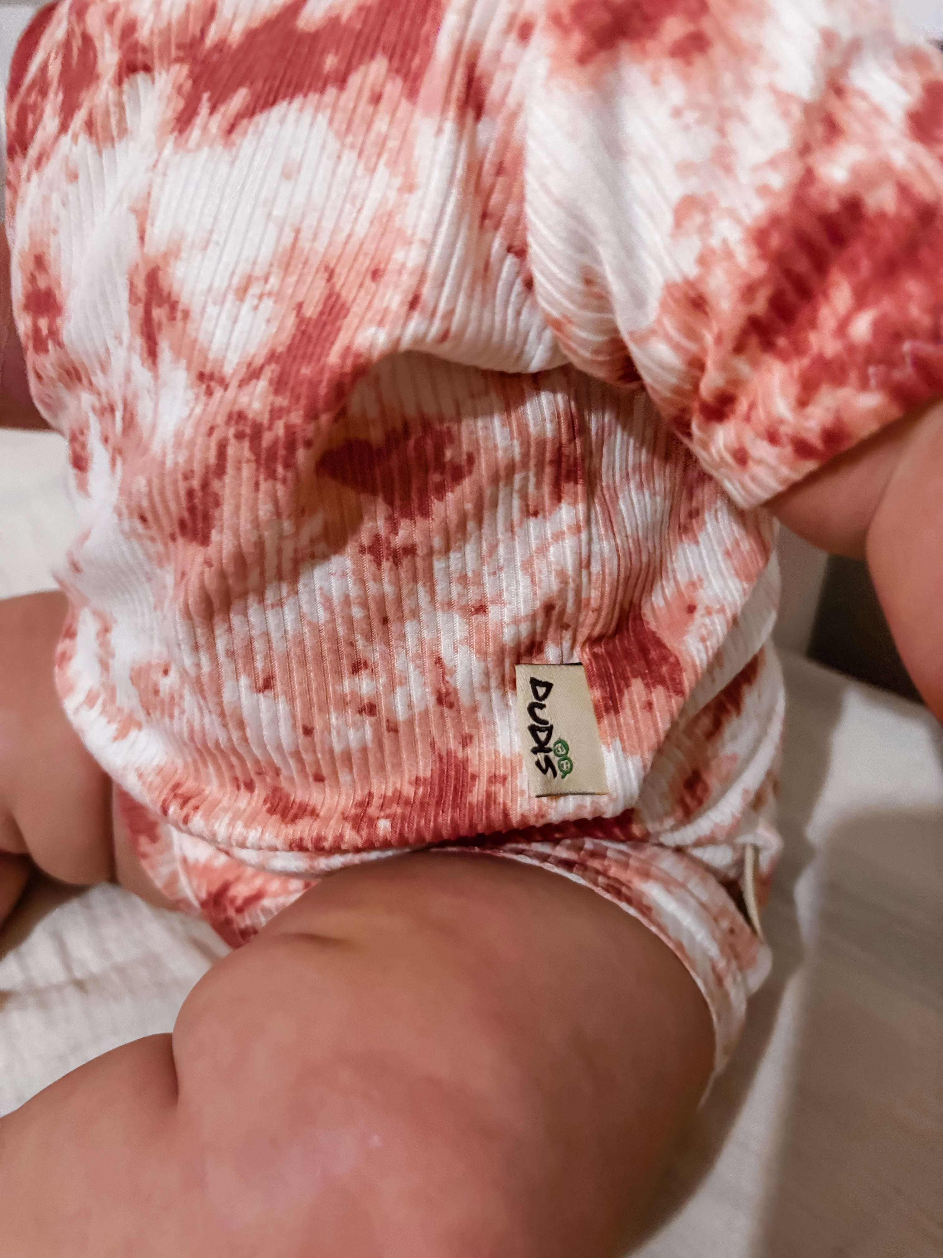 Close-up of a baby wearing a red and white patterned diaper with a visible brand label.