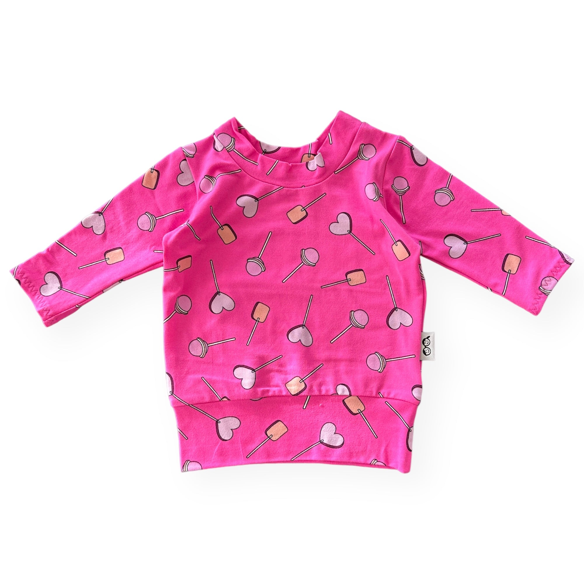 Handmade baby and toddler long-sleeve top featuring a vibrant pink lollipop and heart design. Soft, cozy, and perfect for pairing with leggings or pants for a playful yet comfortable look. Available in sizes preemie to 4T.