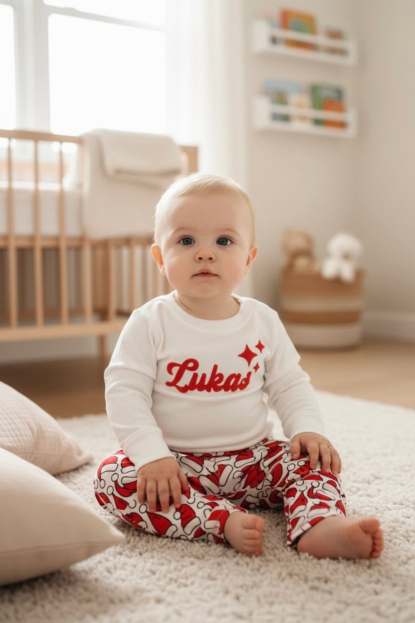 Baby sitting on carpet wearing white personalized sweatshirt with red “Lukas” name and stars.