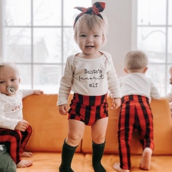 Baby wearing red buffalo plaid bummies and a matching headband, styled with a &
