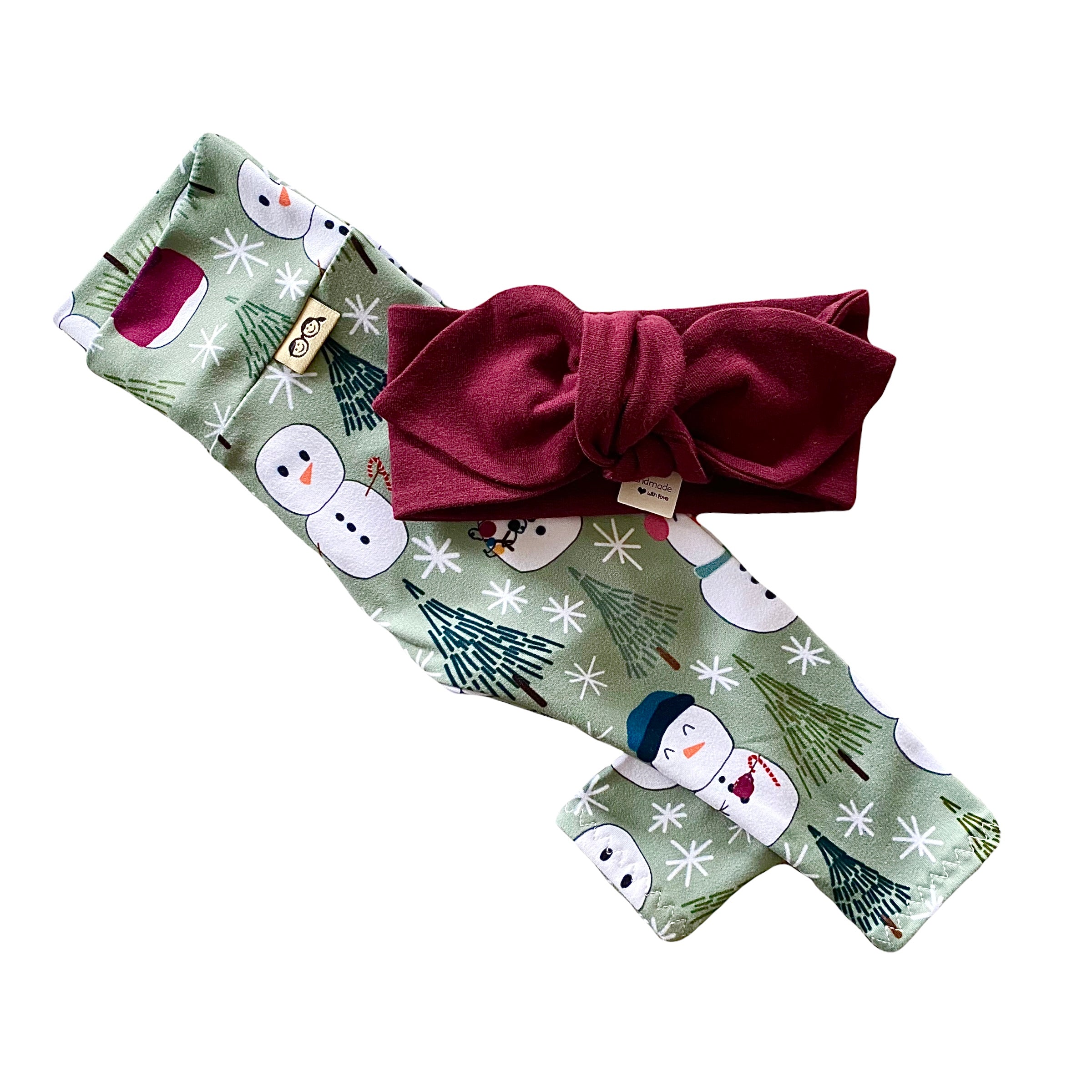 Snowman Print Leggings featuring a playful snowman and winter tree design on a soft green background, paired with a burgundy bow headband. Handmade for babies and toddlers, perfect for holiday celebrations and seasonal outfits.