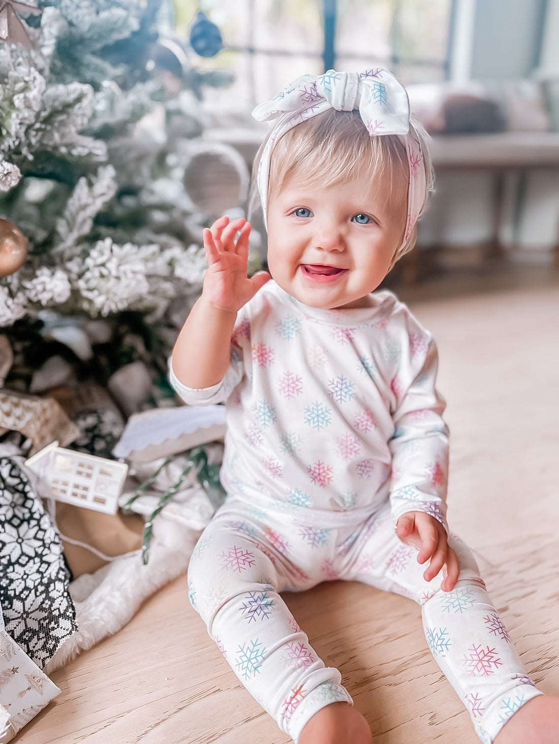 Child in a snowflake lounge set sitting in front of a decorated Christmas tree.