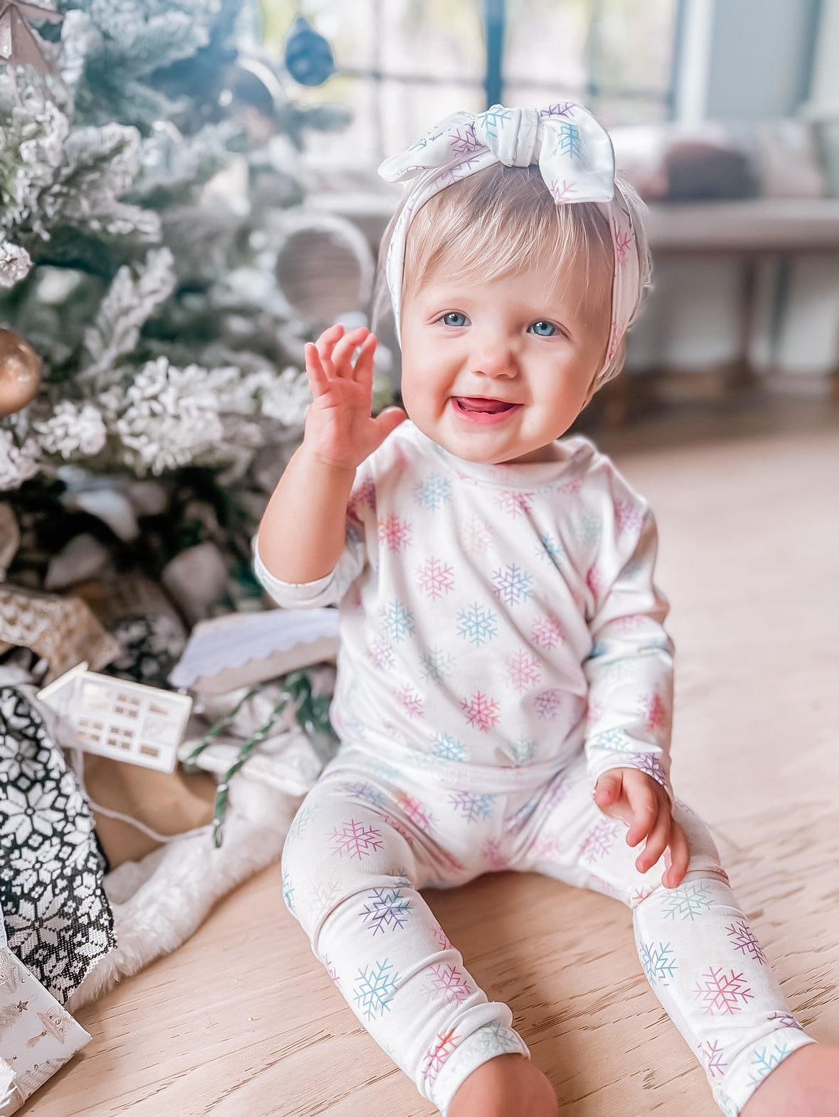 Child in a snowflake lounge set sitting in front of a decorated Christmas tree.