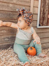 Baby sitting on straw with a pumpkin, wearing a headband and romper, against a wooden background.