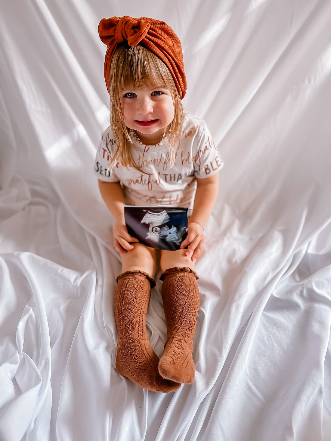 Child wearing a turban and holding an ultrasound image on a white background