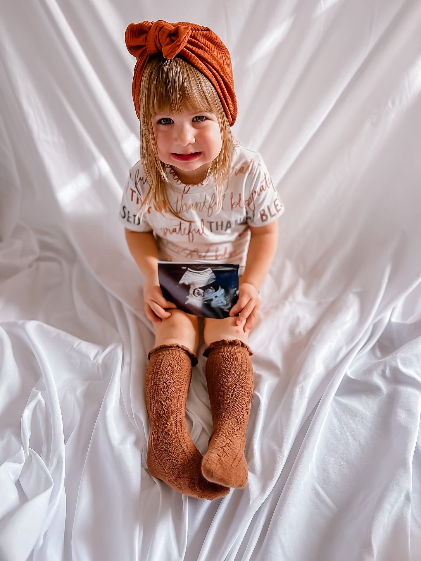 Child wearing a turban and holding an ultrasound image on a white background