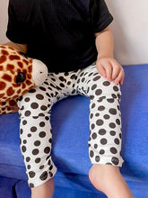 Close-up of white baby leggings with black polka dots, shown on a toddler seated on a blue couch. Soft, stretchy, and perfect for everyday wear or gifting, these handmade baby pants are ideal for boys and girls.