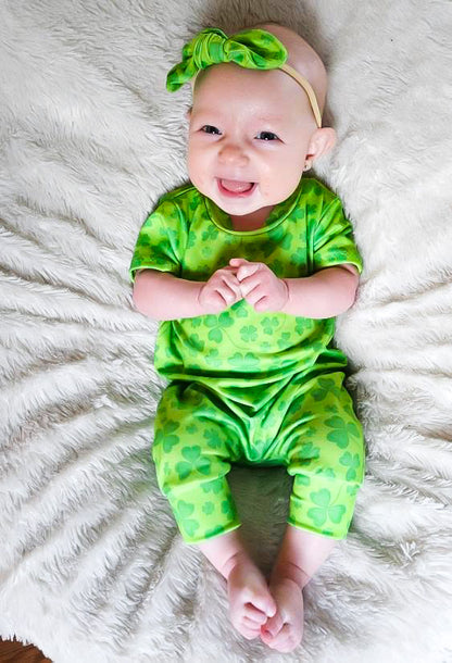 Smiling baby wearing green shamrock romper with matching bow – Lucky clover baby outfit for St. Patrick’s Day celebrations, first holiday outfits, and festive baby photoshoots.