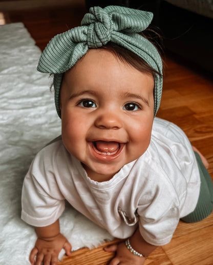 Happy baby crawling while wearing ribbed green leggings, a matching bow headband, and a white floral-pocket tee.