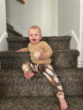 Baby sitting on a carpeted staircase holding a ball in Beige camel  textured sweater 