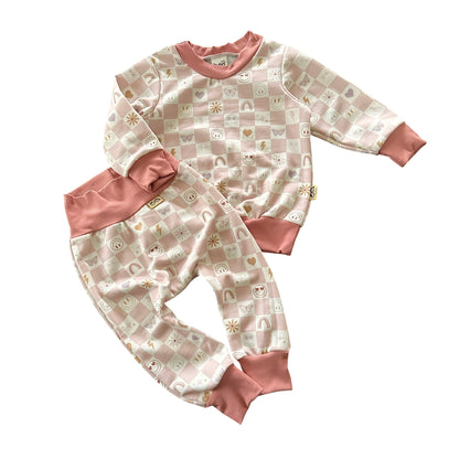 Baby lounge set in blush pink checker print with smiley faces and icons, front view top and pants.
