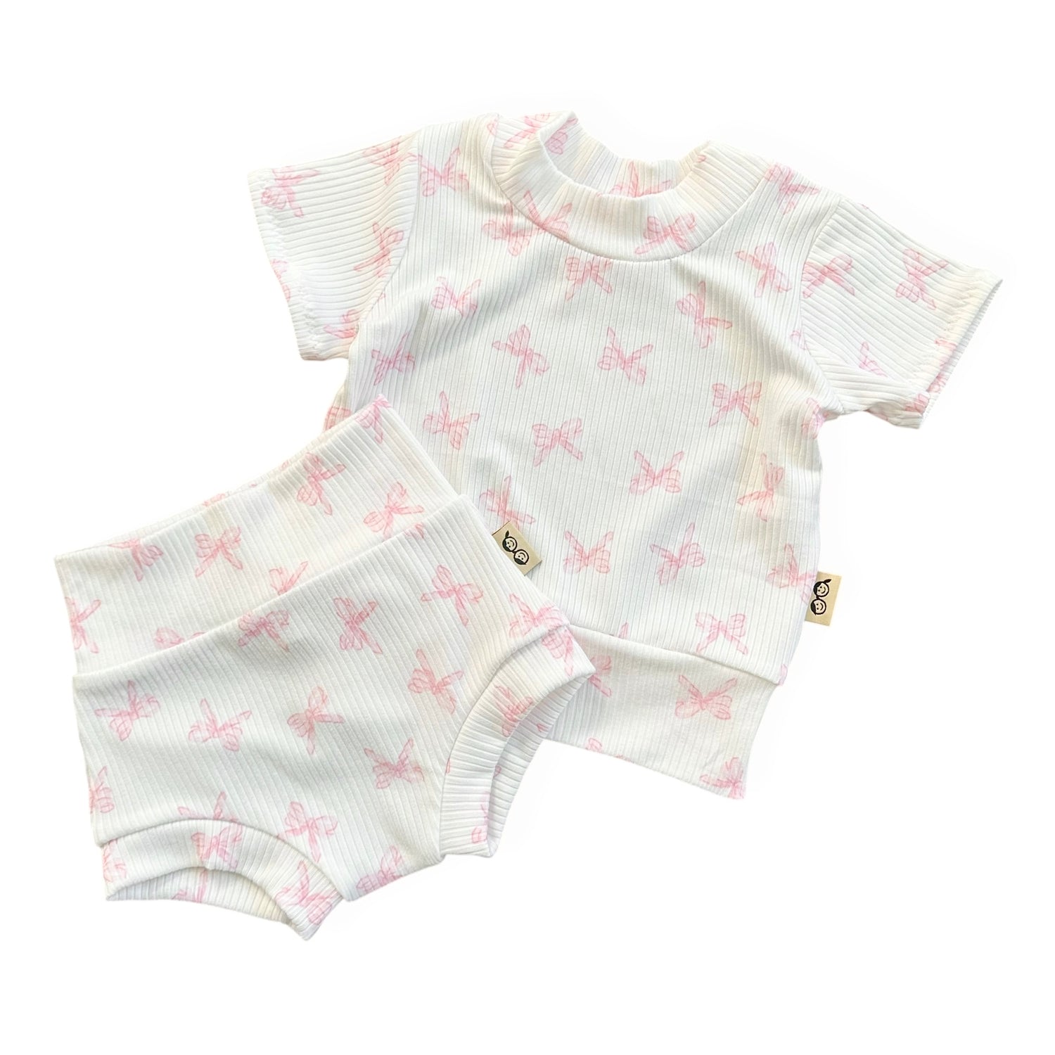 Baby outfit with short-sleeve top and shorts featuring pink bow pattern on a white background