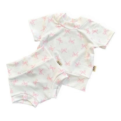 Baby outfit with short-sleeve top and shorts featuring pink bow pattern on a white background