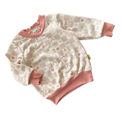 Angled flat lay of blush checker sweatshirt for babies with smiley icons.