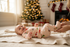 Smiling baby in retro Christmas lounge set lying on blanket with tree lights in the background – soft handmade outfit.