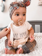 Cute baby wearing Retro Plaid Leggings and a matching bow headband, holding a wooden toy camera, paired with a stylish onesie.