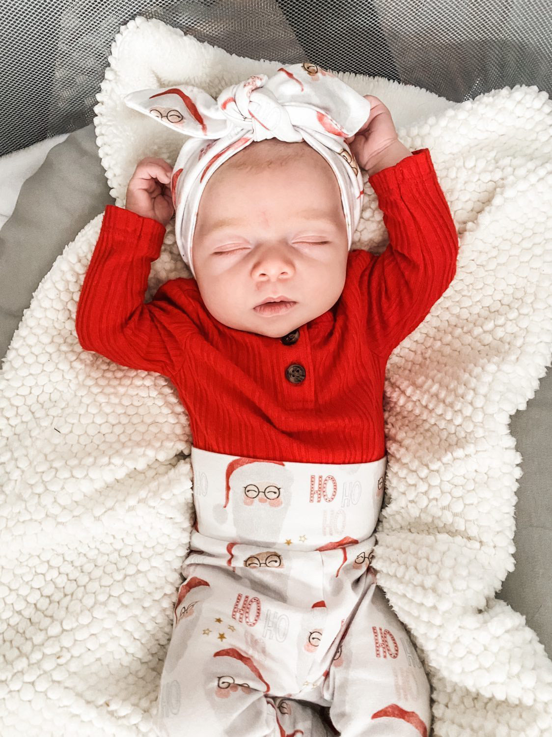 Sleeping newborn dressed in Vintage Santa leggings and a matching bow headband, paired with a red ribbed top. Cozy and festive holiday look for babies.